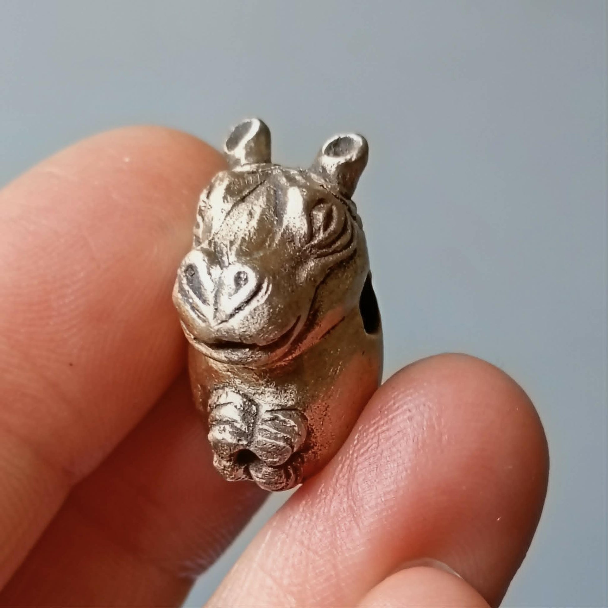 En bronspärla som ser ut som en flodhäst skulpterad i brons hålls fram mellan fingrar