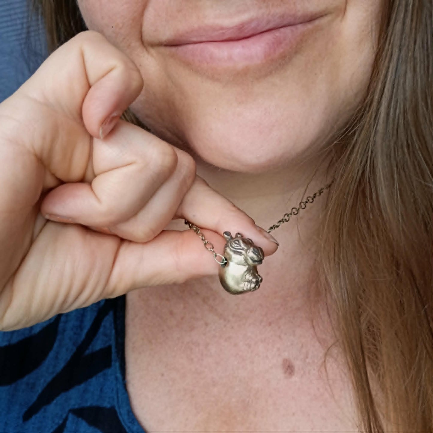 Sculptor Anna Siivonen holding her handmade bronze hippo pendant close to their face