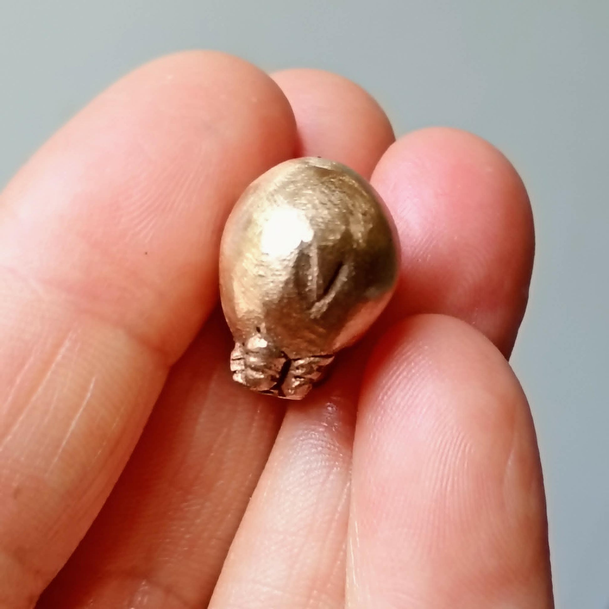 En bronspärla som ser ut som en flodhäst, sedd bakifrån, visar en liten svans och rumpa,  skulpterad i brons hålls fram mellan fingrar