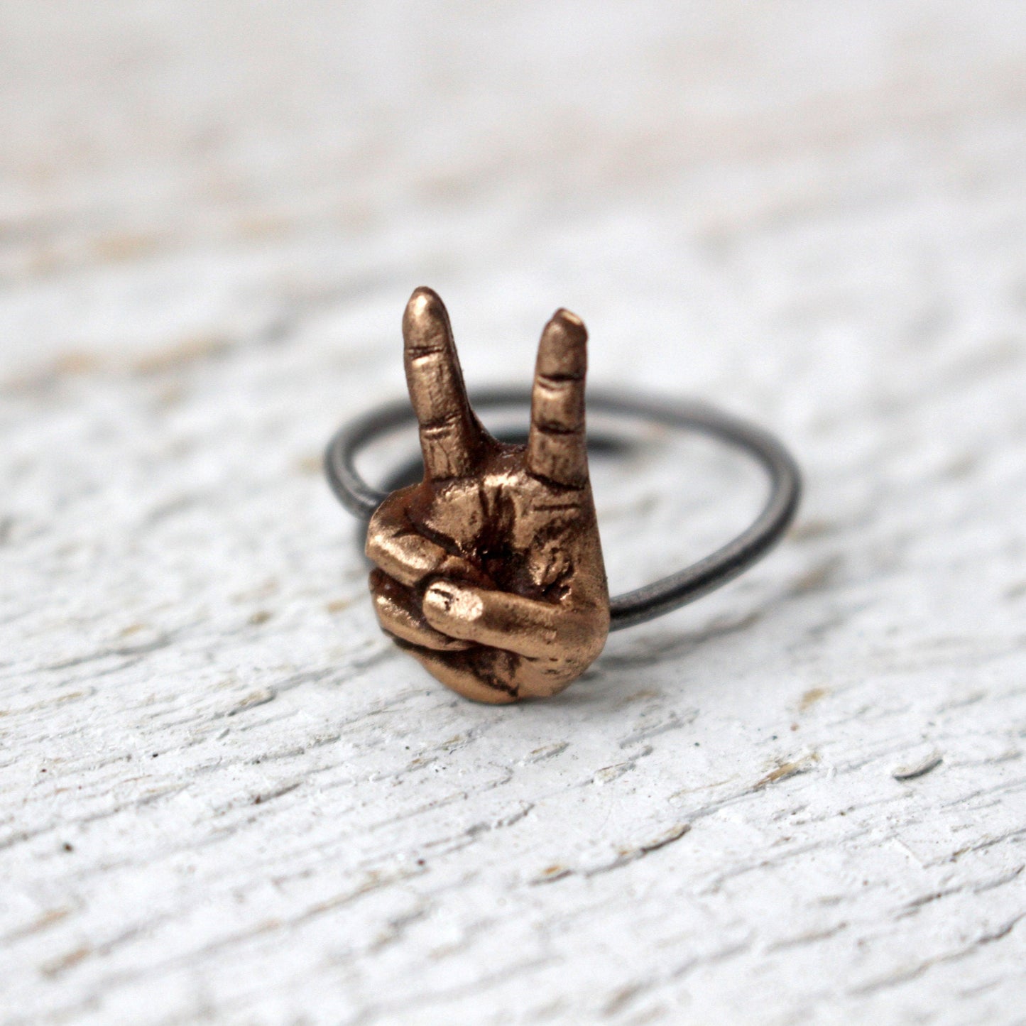 ring i brons och rostfritt stål med en hand som gör segertecken eller fredstecken