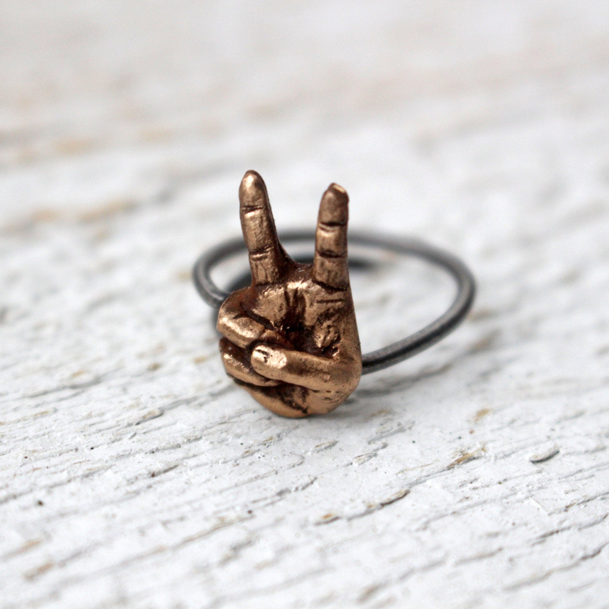 ring i brons och rostfritt stål med en hand som gör segertecken eller fredstecken