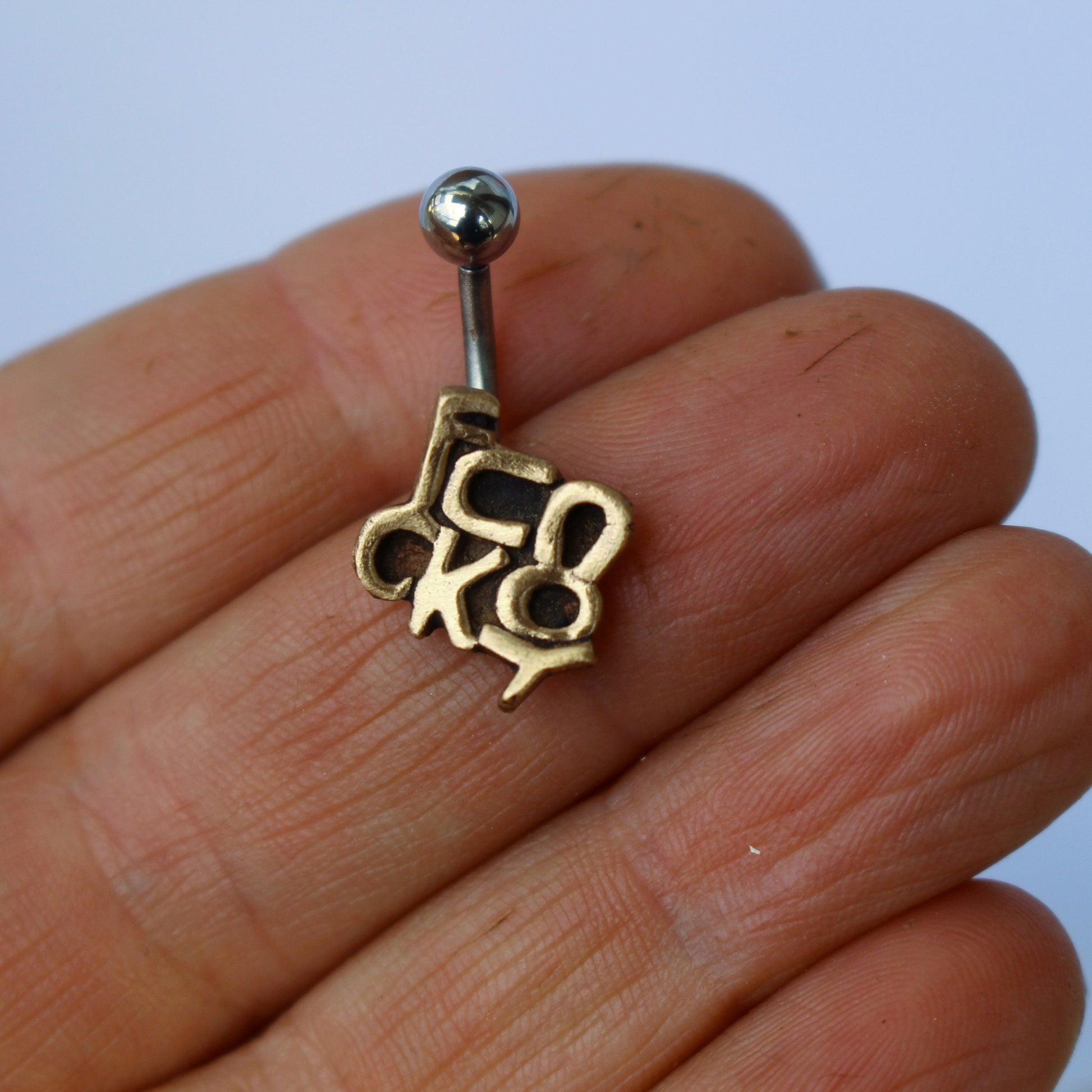 navelpiercing smycke med texten fuck you skulpterat i brons