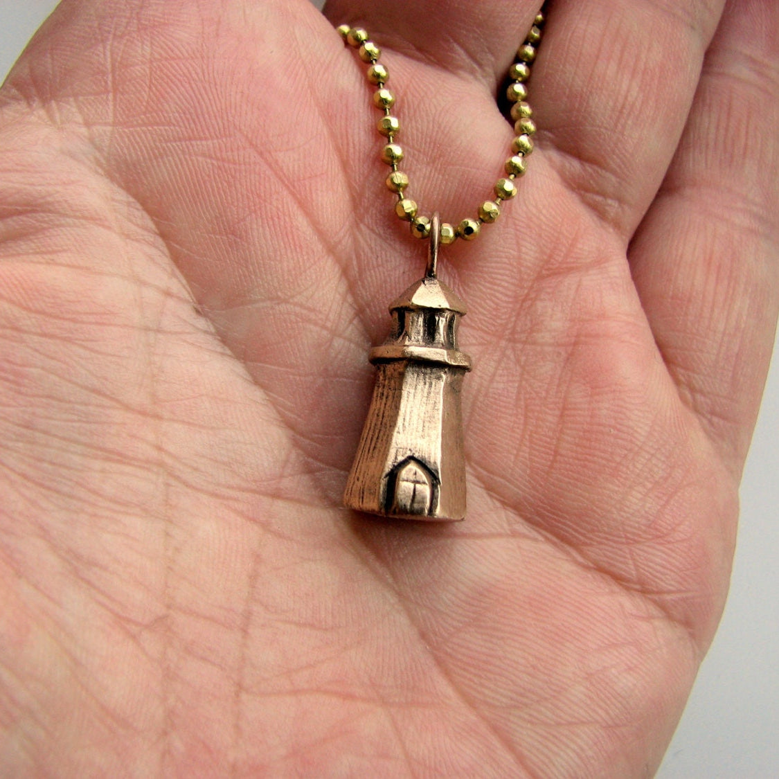 Halsbands hänge med en liten fyr skulpterad i brons