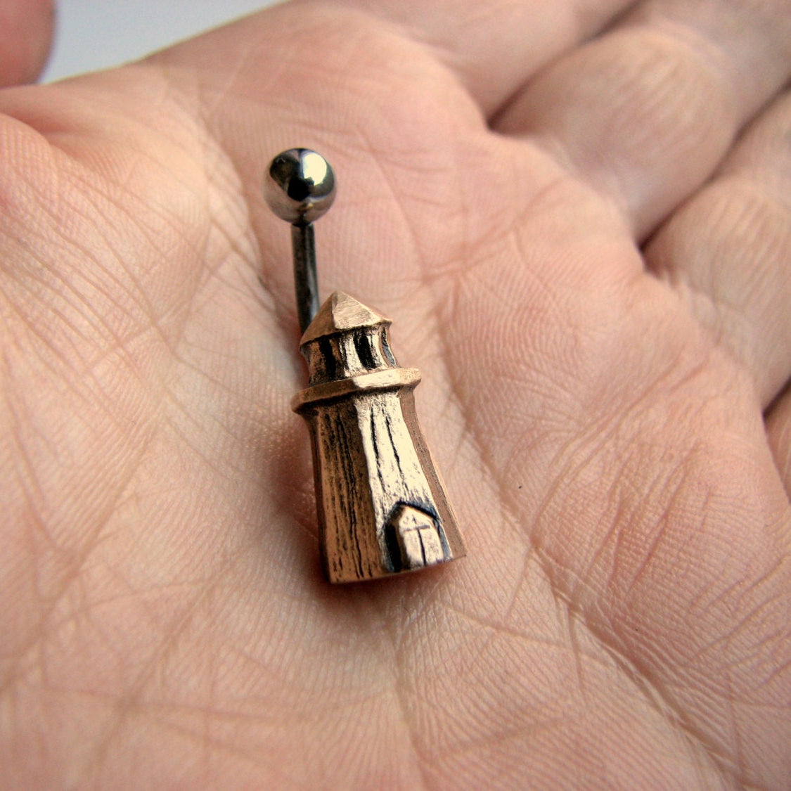 Navelring i titan med en liten skulpterad brons fyr