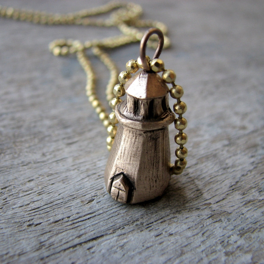 Halsbands hänge med en liten fyr skulpterad i brons