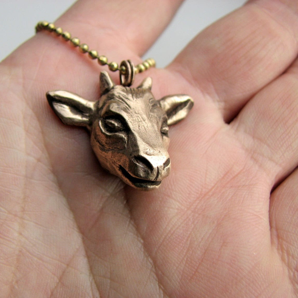 Bronze goat pendant on a chain held in a hand