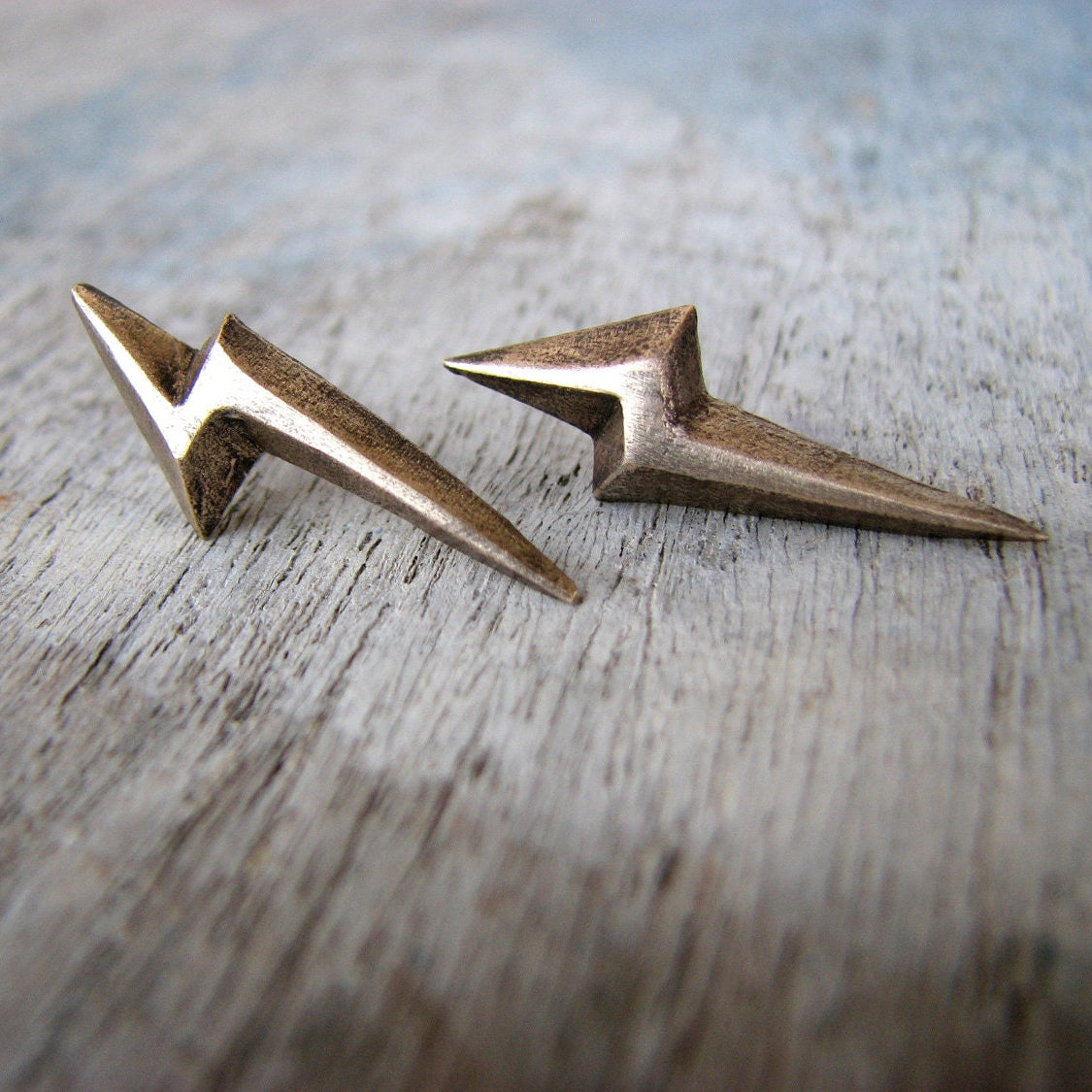 Pair of bronze lightning bolt-shaped earrings on a wooden surface