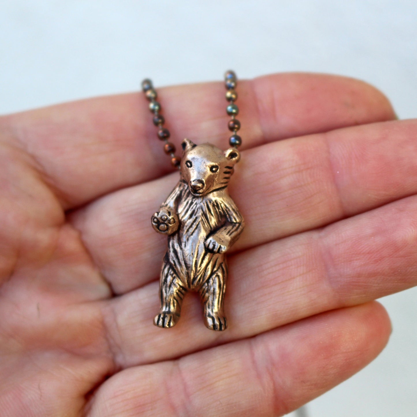 halsband med en liten björn som ser ut som att den vinkar med ena tassen, nalle hänge