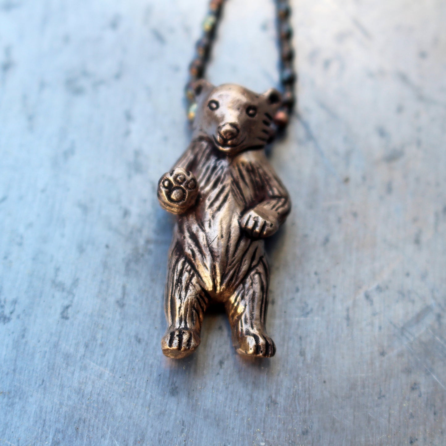 A bronze necklace featuring a miniature bear standing on its hind legs with an oxidized stainless steel ball chain.