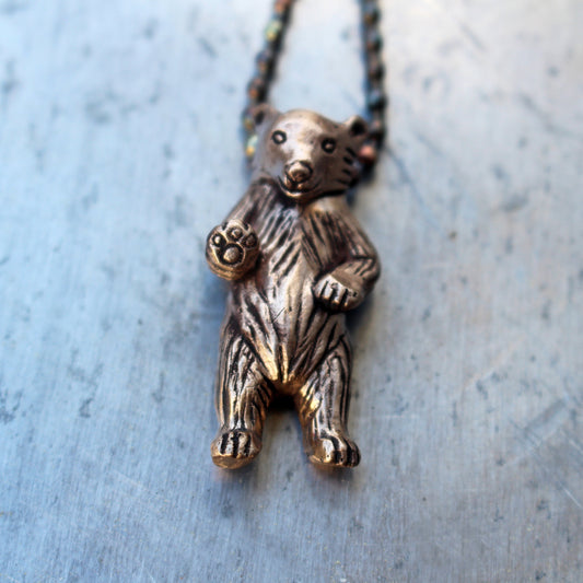 A bronze necklace featuring a miniature bear standing on its hind legs with an oxidized stainless steel ball chain.