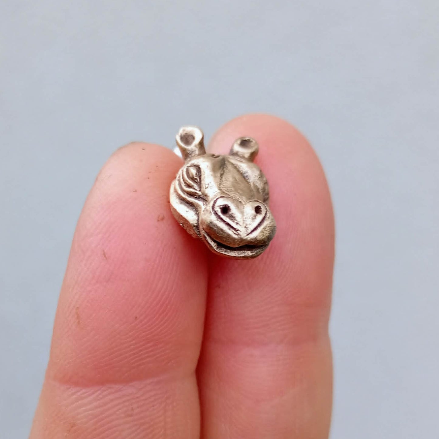 flodhäst piercing smycke i brons och titan hållen mellan fingrar
