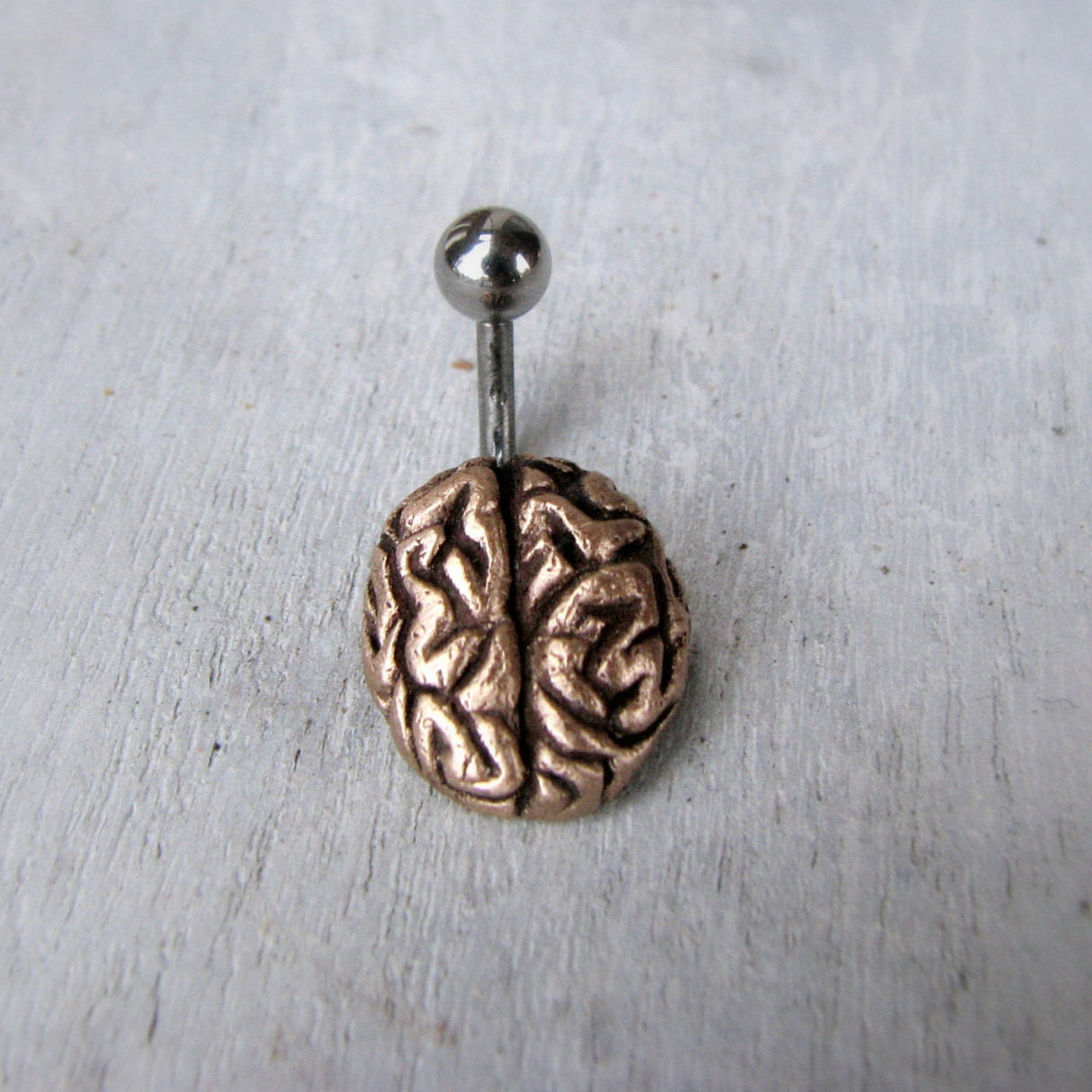 Navelpiercing smycke med en liten skulpterad hjärna i brons och titan stång