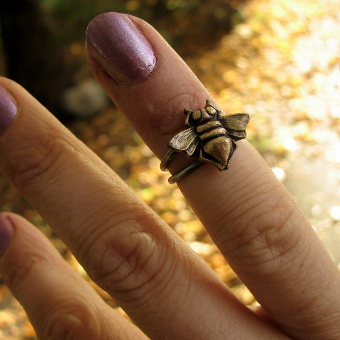 A bronze honey bee ring attached to a stainless steel band, worn on a person's finger.