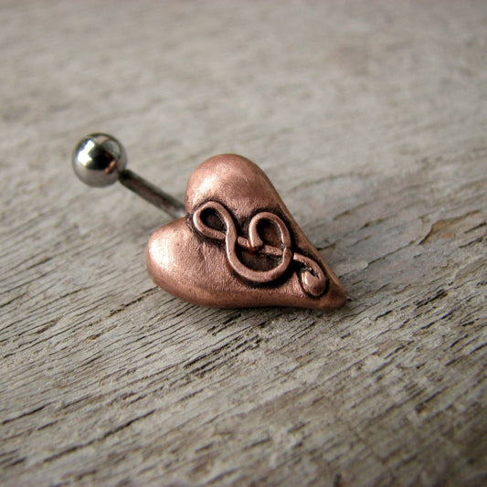 A belly button ring with a puffy heart in pink copper and a g clef design on it, attached to a curved barbell.