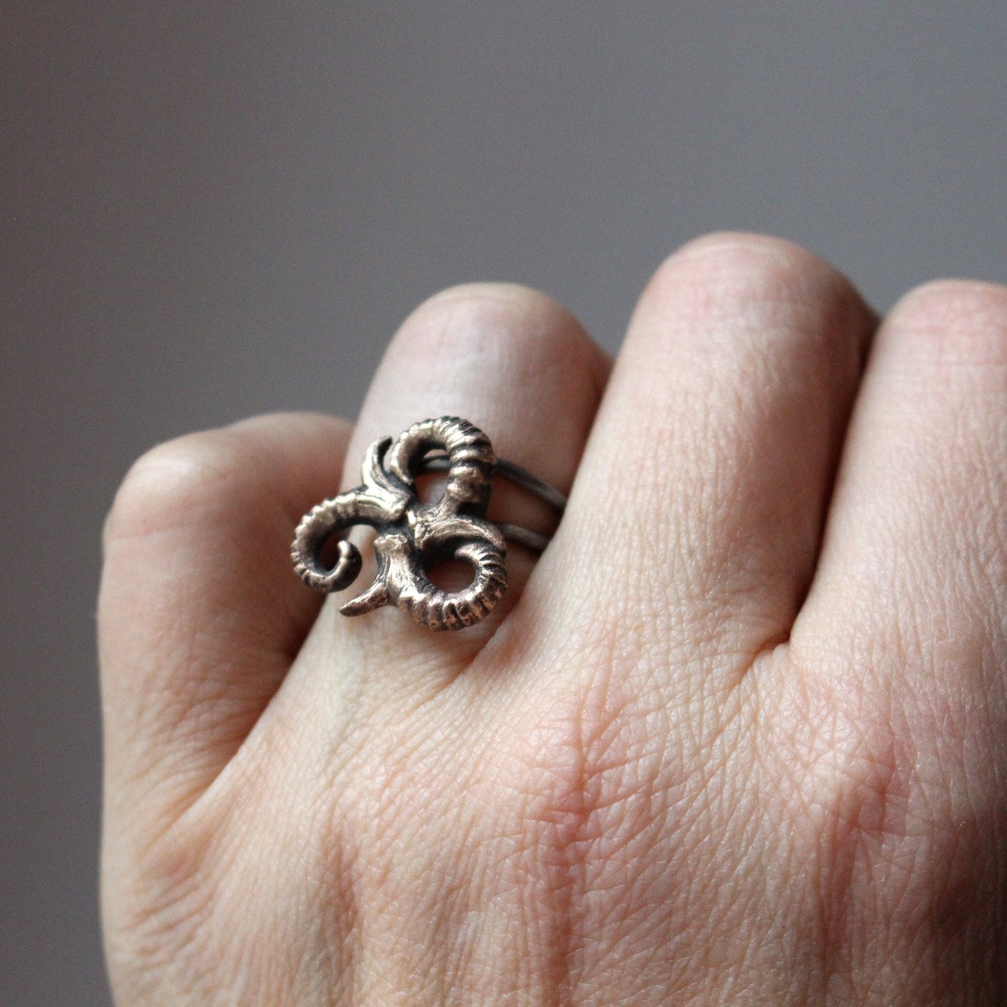 A hand wearing a bronze and stainless steel triskelion ring with an adjustable band, featuring a three-swirl design resembling antlers.