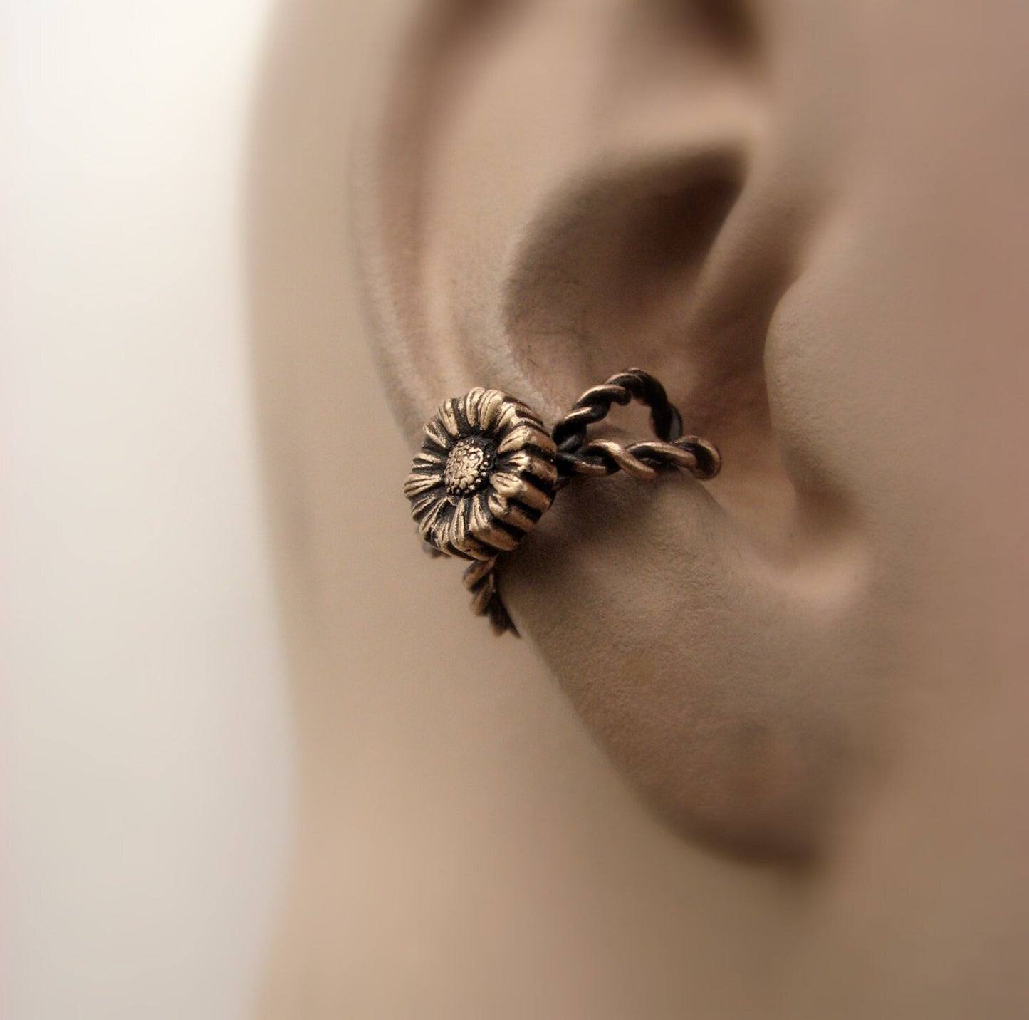 An ear cuff featuring a golden sunflower design displayed on a mannequin ear.