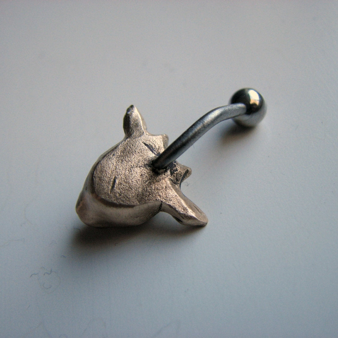 baksida, navelpiercingsmycke med ett gethuvud skulpterat i brons, stav i titan eller kirurgiskt stål