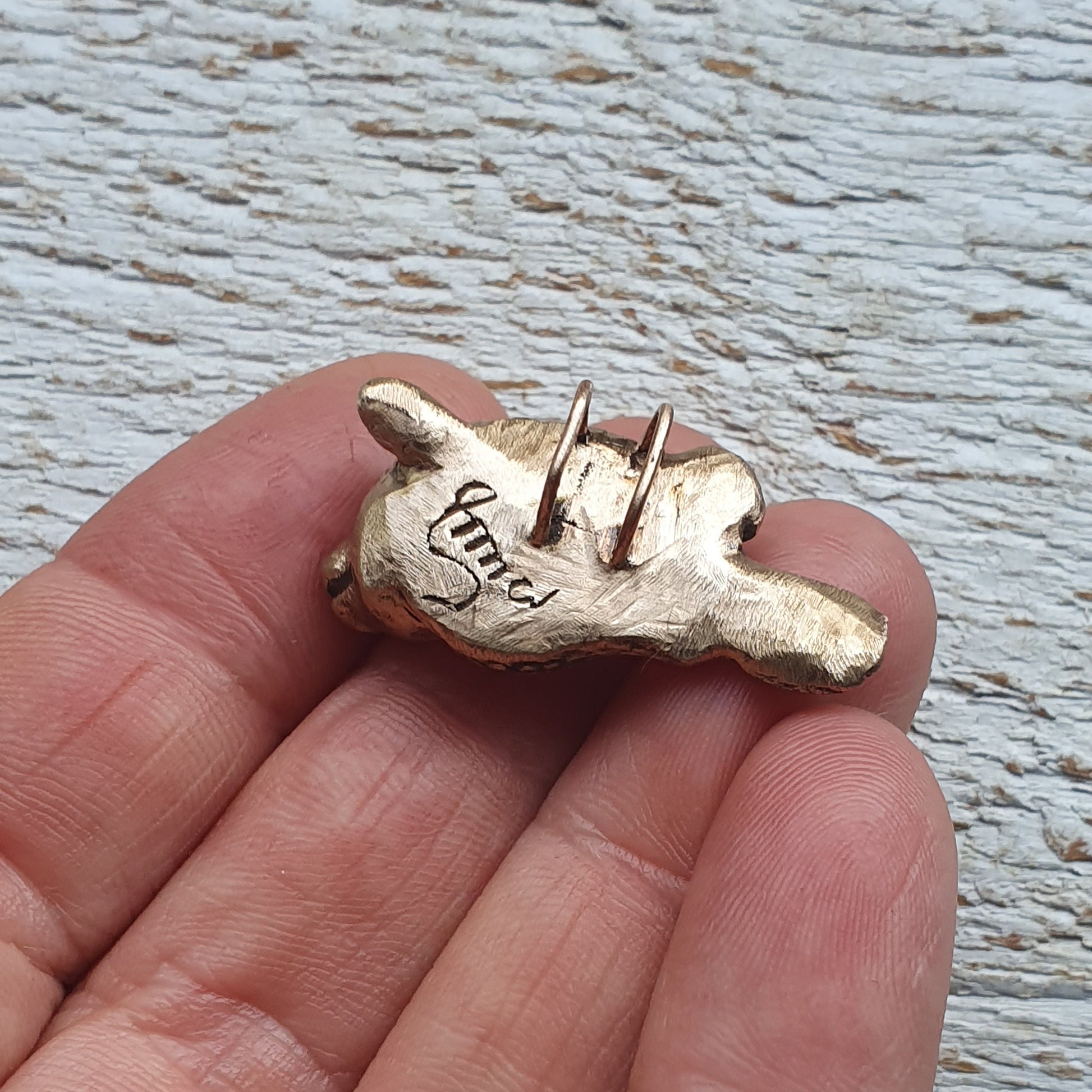 baksida, kofisk skulpterat i brons, smycke med en ko med fiskkropp med en fyrklöver bakom ena örat