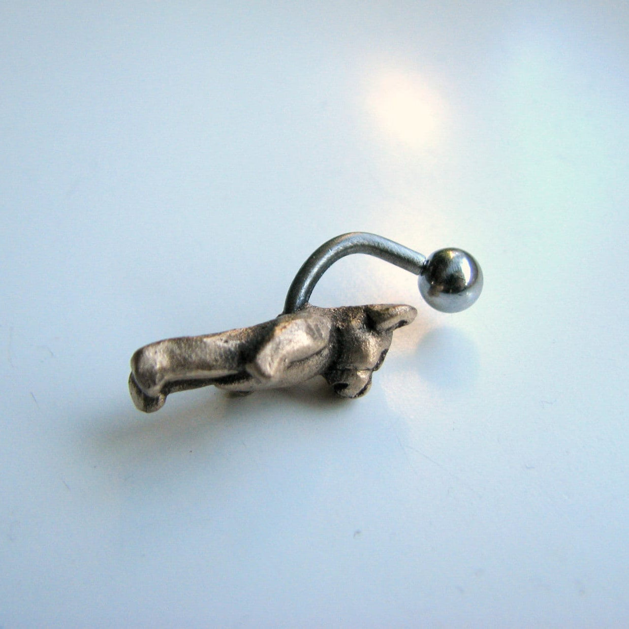 Metallic belly button ring with a teddy bear on a light blue background