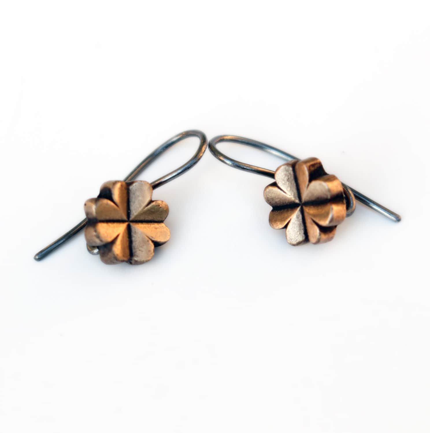 A pair of clover-shaped dangle earrings with bronze leaves and niobium or titanium wires on a white background.