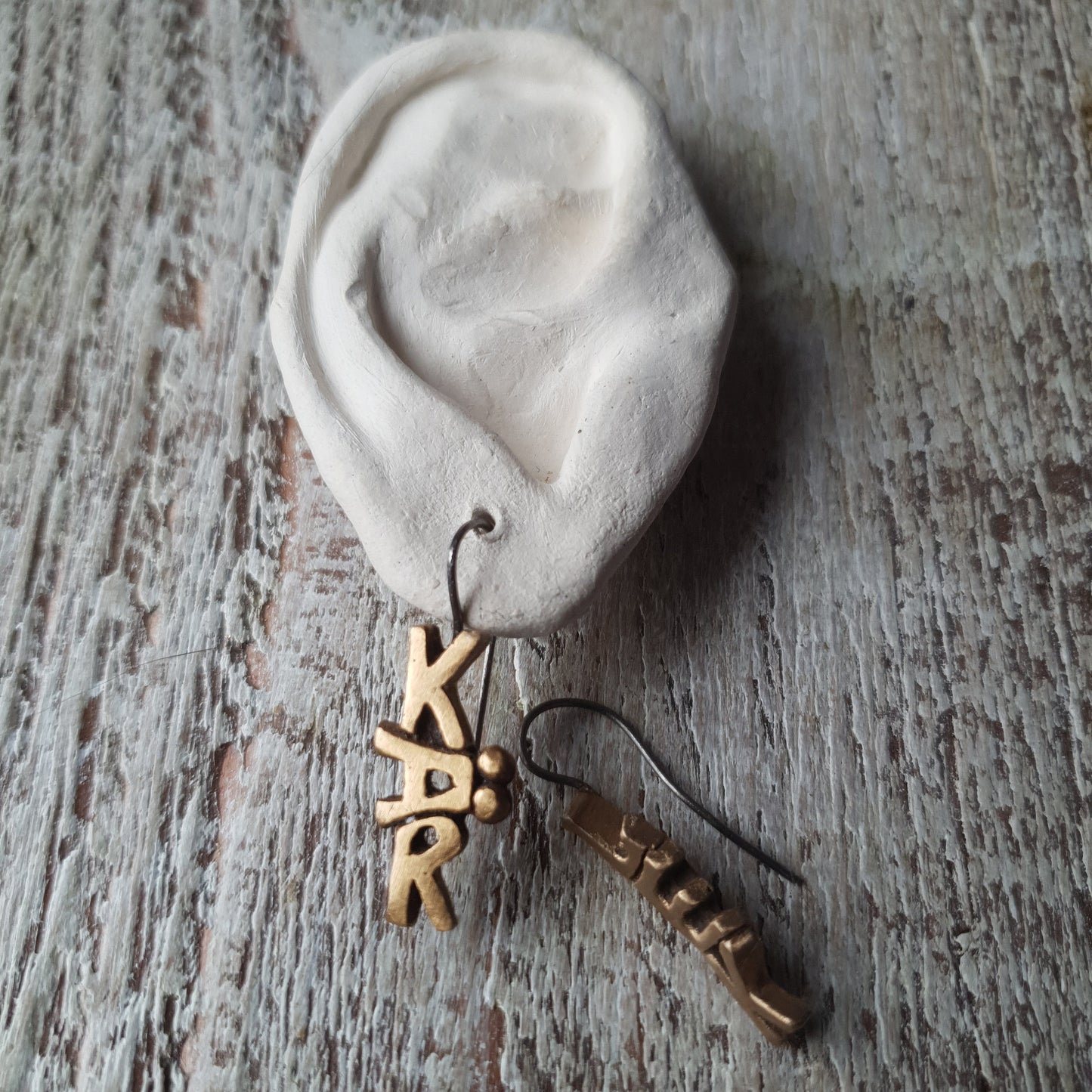 hängande örhängen med skulpterade bokstäver, på det ena står det kär det andra lek