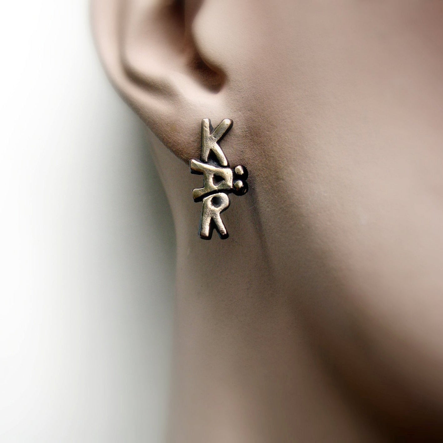 ett örhänge på modells öra, örhänget har skulpterade bokstäver, det står lek