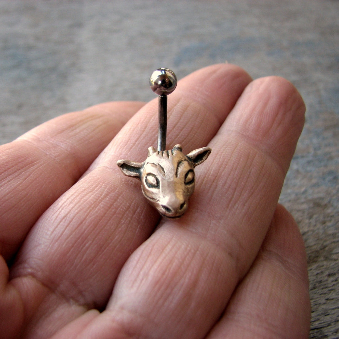 navelpiercingsmycke med ett gethuvud skulpterat i brons, stav i titan eller kirurgiskt stål