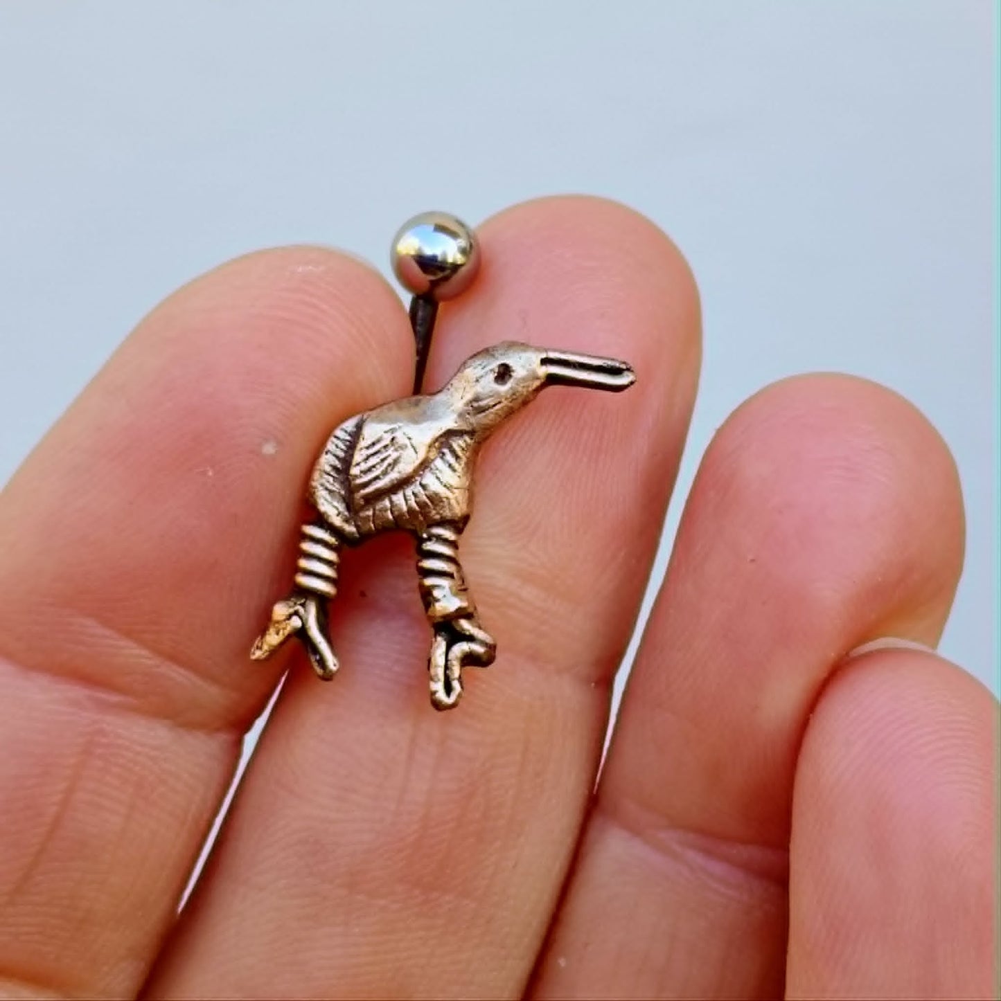kiwifågel navel piercing smycke i brons och titan, i en persons hand