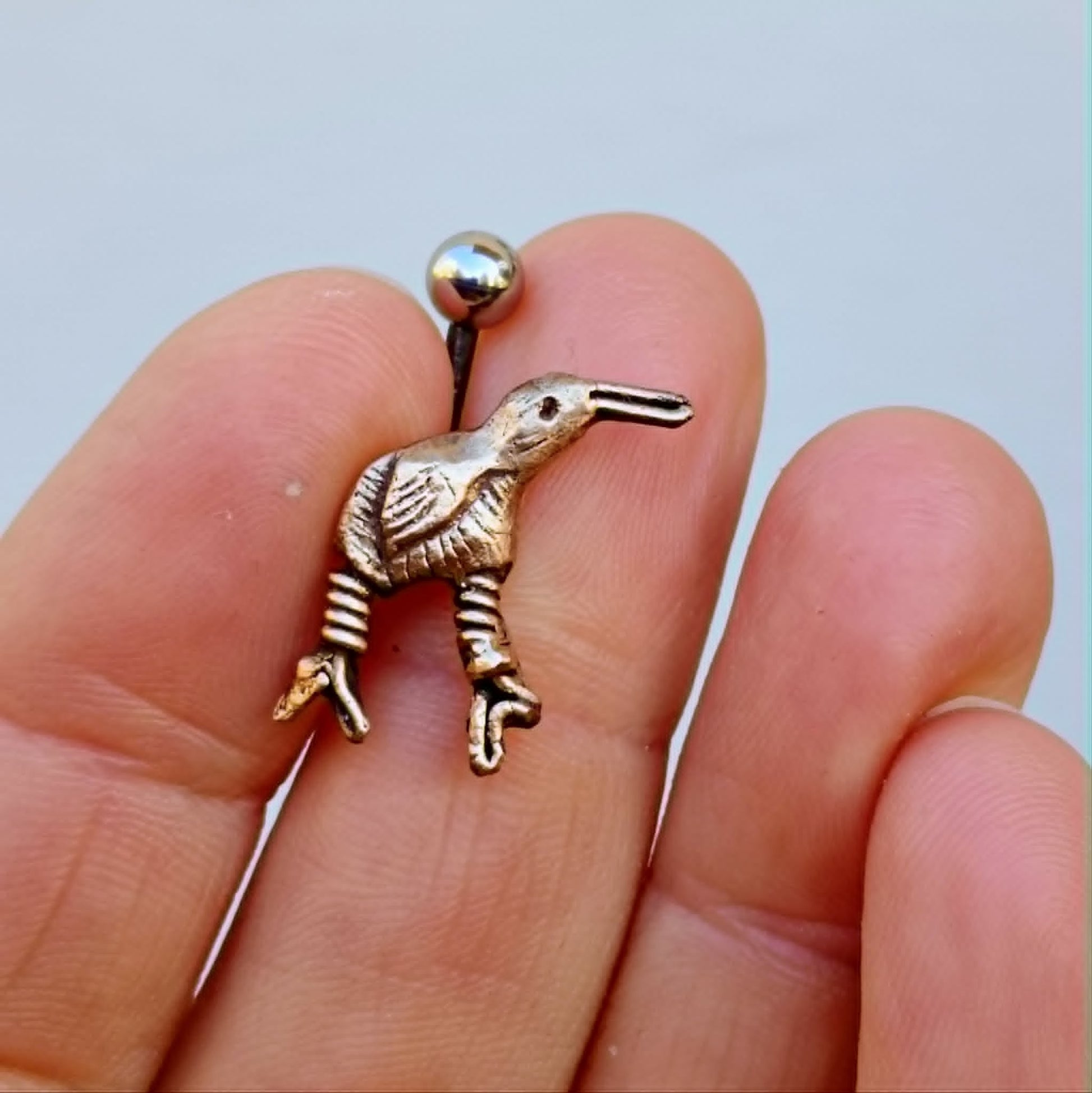 kiwifågel navel piercing smycke i brons och titan, i en persons hand