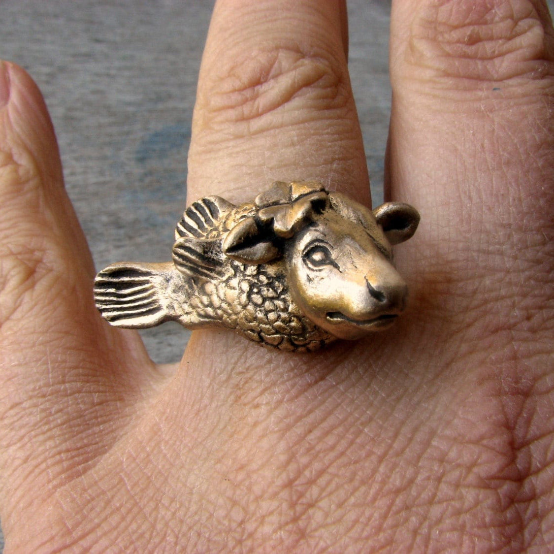fingerring, skulpterat i brons och stål, föreställande en ko med fiskkropp med en fyrklöver bakom ena örat 
