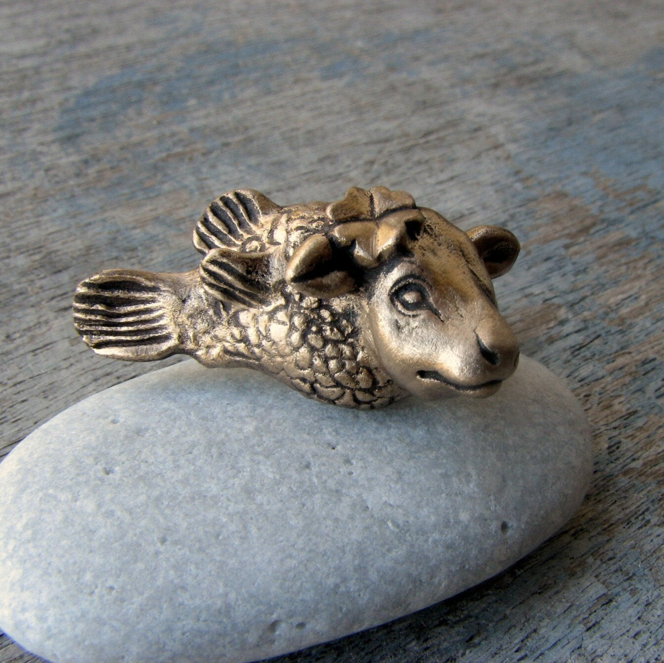 kofisk skulpterat i brons, smycke med en ko med fiskkropp med en fyrklöver bakom ena örat