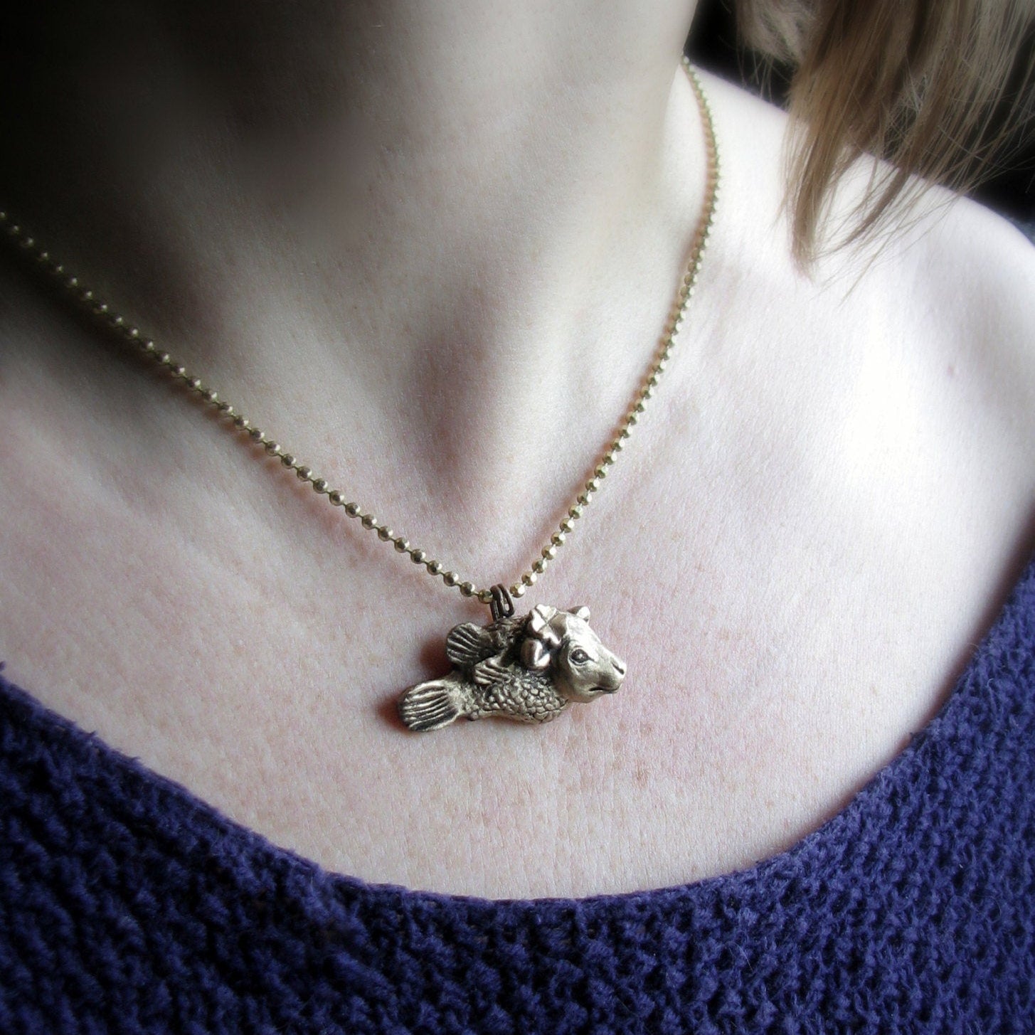 kofisk skulpterat i brons, smycke med en ko med fiskkropp med en fyrklöver bakom ena örat