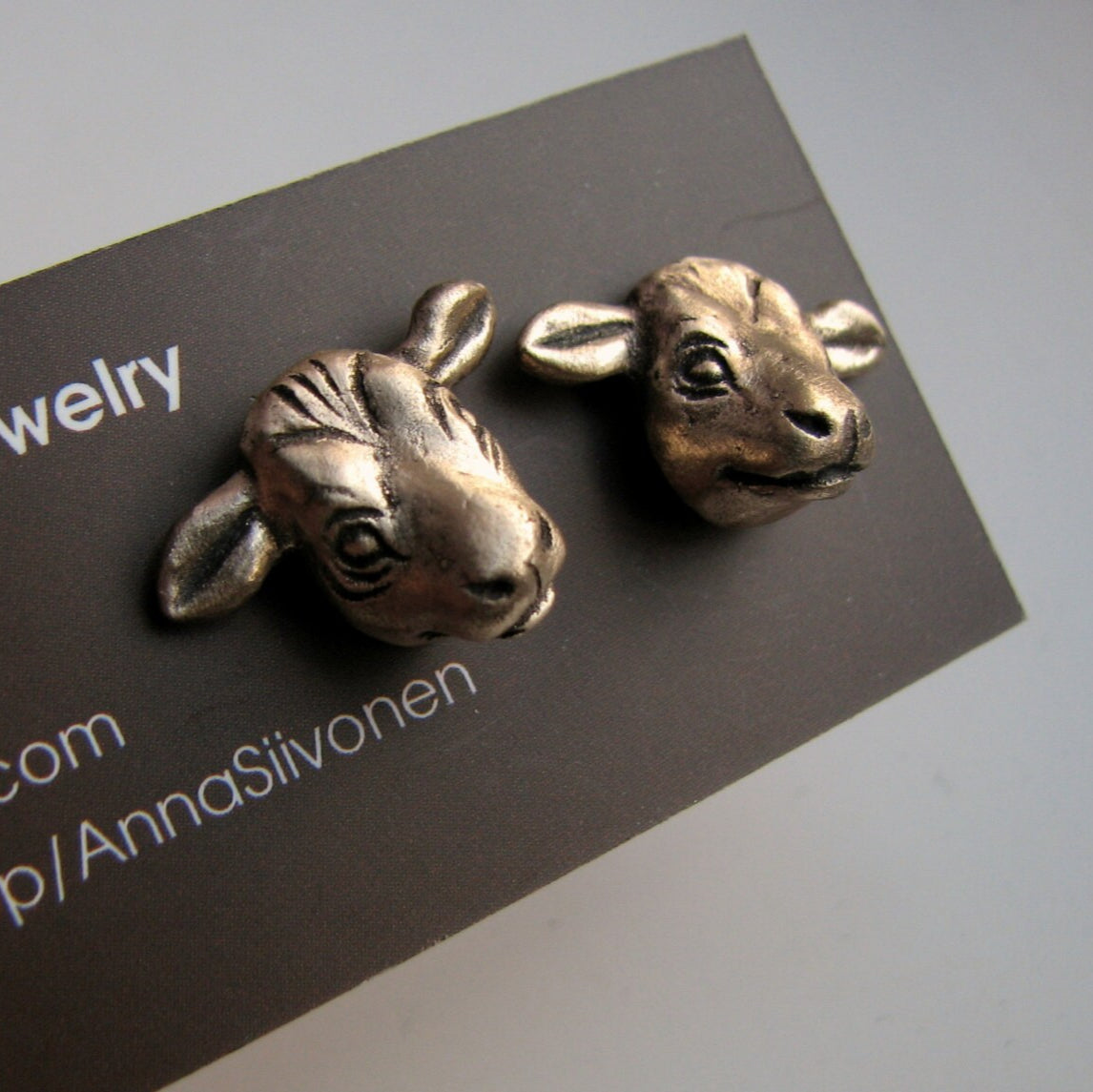A pair of bronze cow head earrings displayed on a dark card with the text 'art jewelry' printed on it.