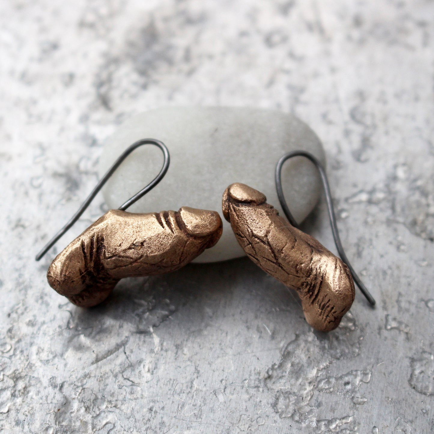 örhängen, med titan krokar, föreställande erigerade kukar skulpterade i brons
