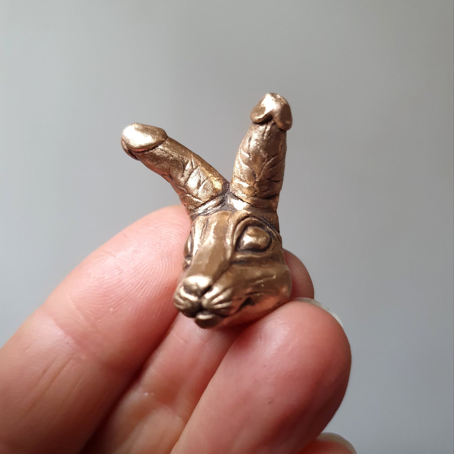 miniatyr figur i brons föreställande ett  kaninhuvud med kukar som öron, som halsband , ring eller brosch