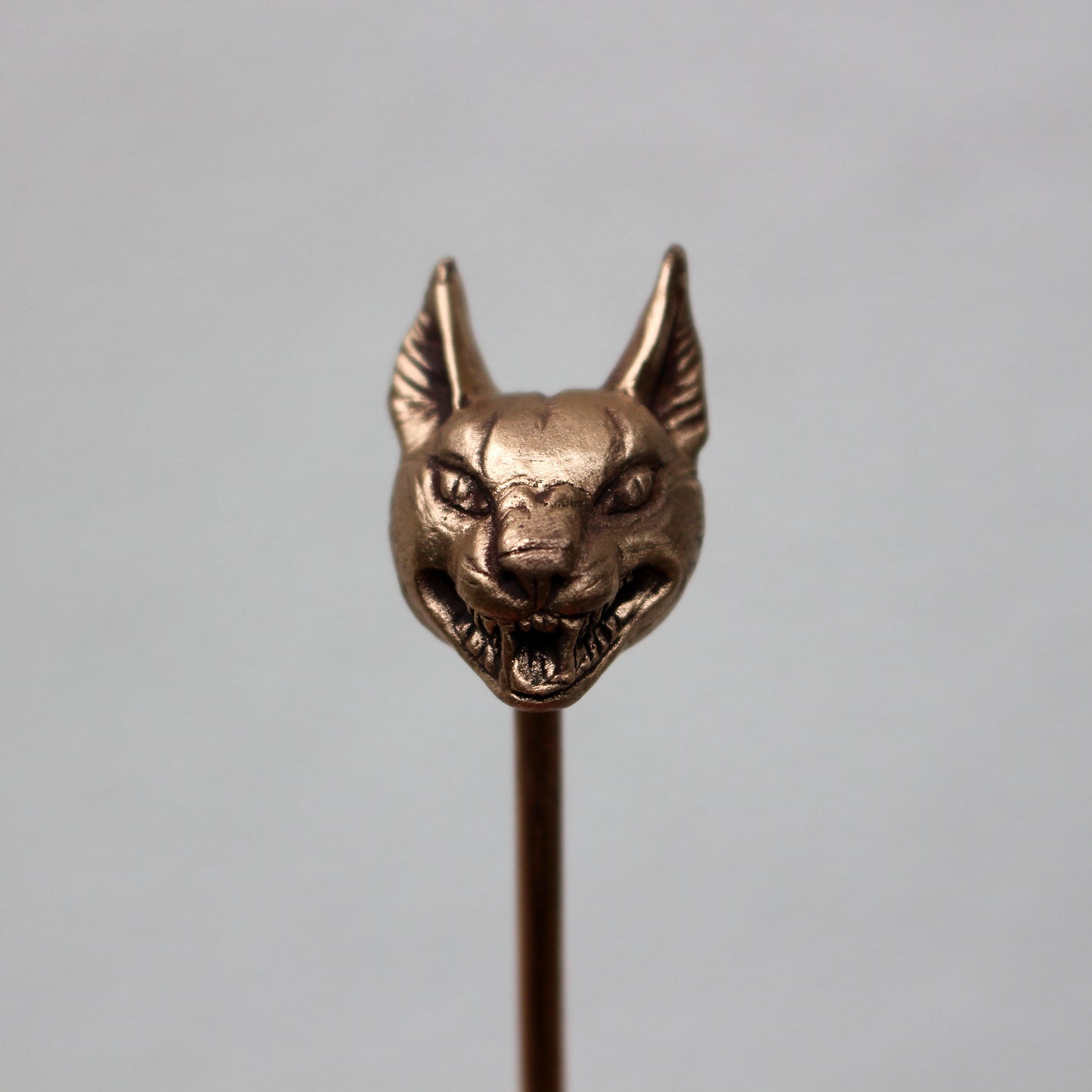 A bronze hair stick with a sculpted wild cat head at the top, displayed against a light background.