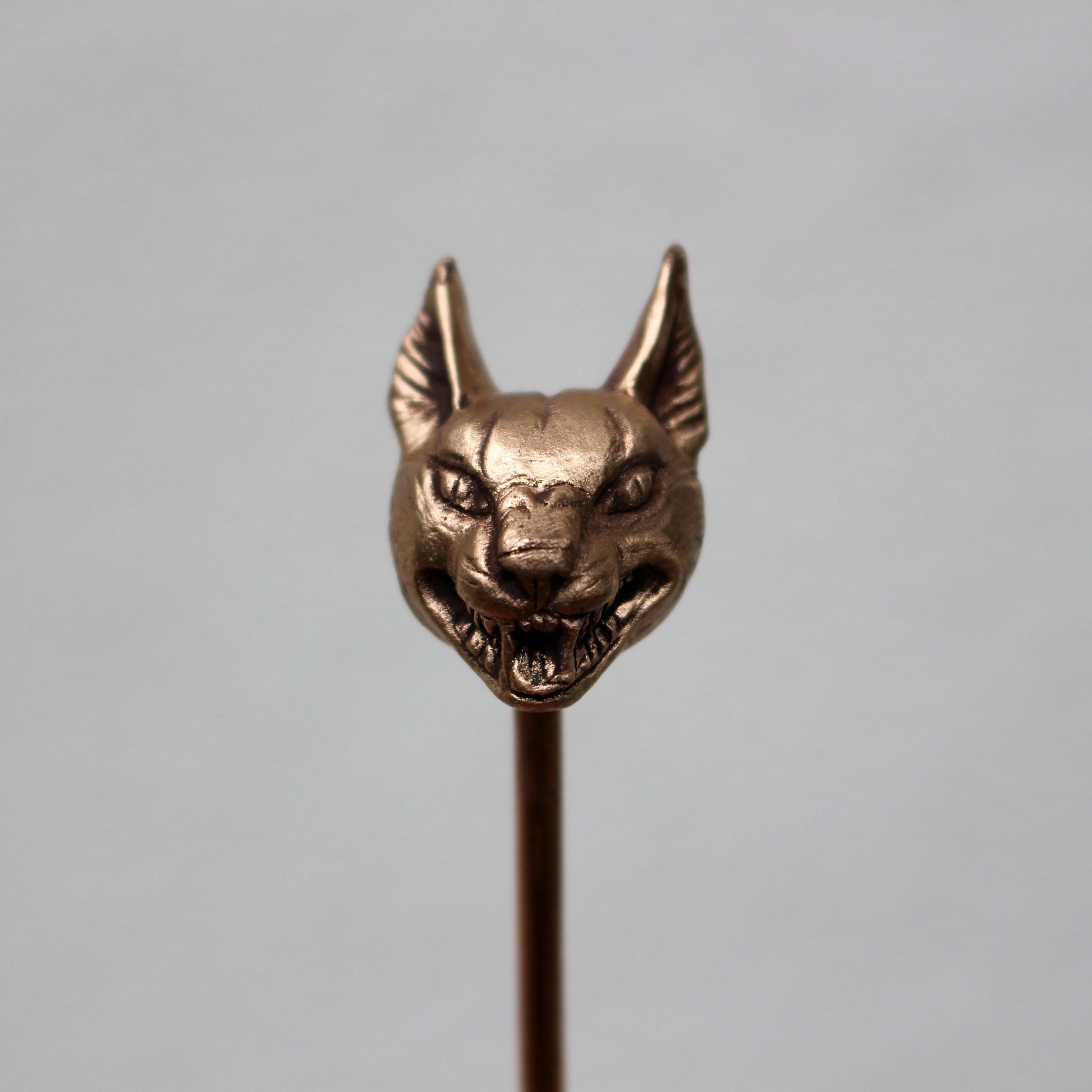 A bronze hair stick with a sculpted wild cat head at the top, displayed against a light background.