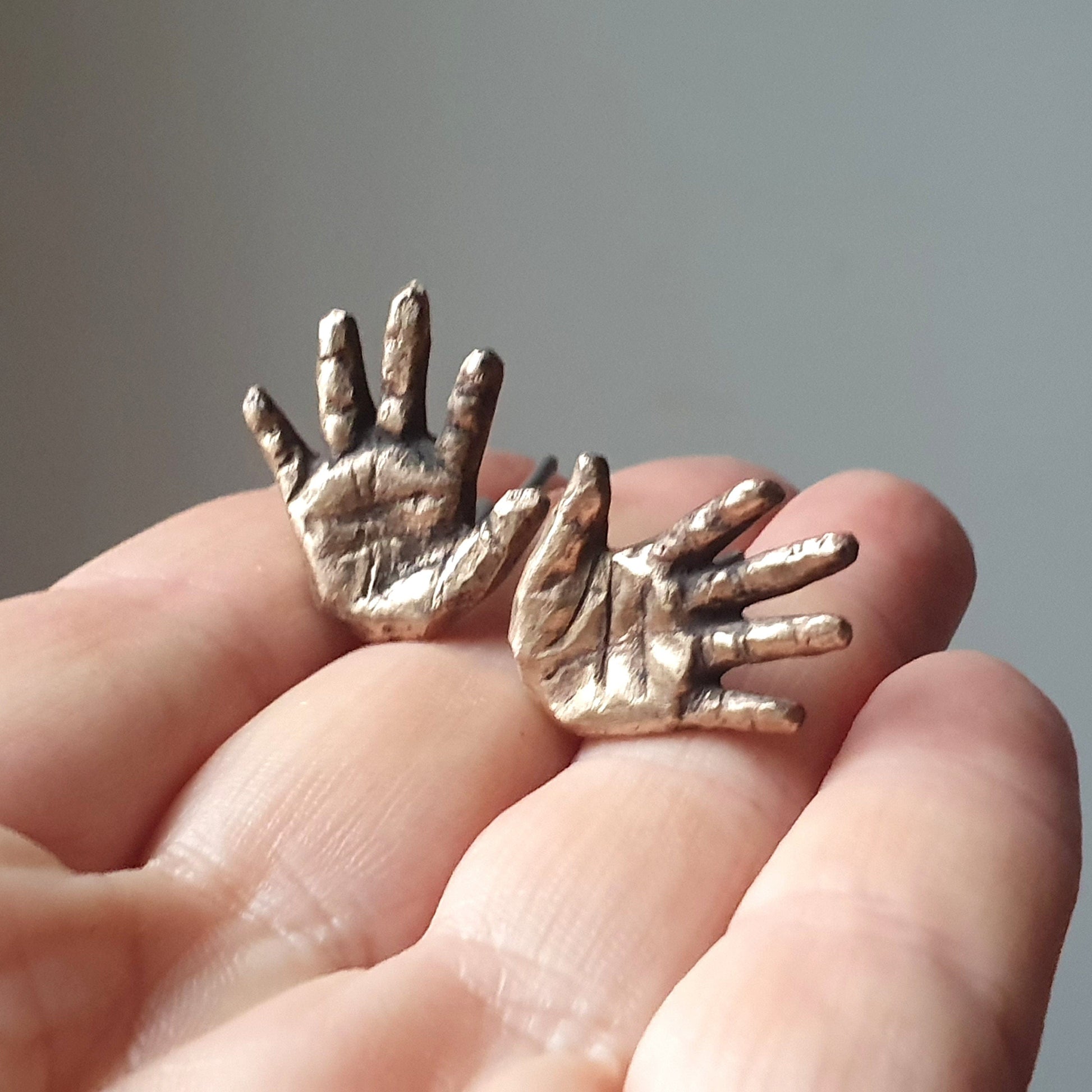 A pair of miniature hand-shaped cufflinks in bronze held in a person's hand, with a detailed and realistic design