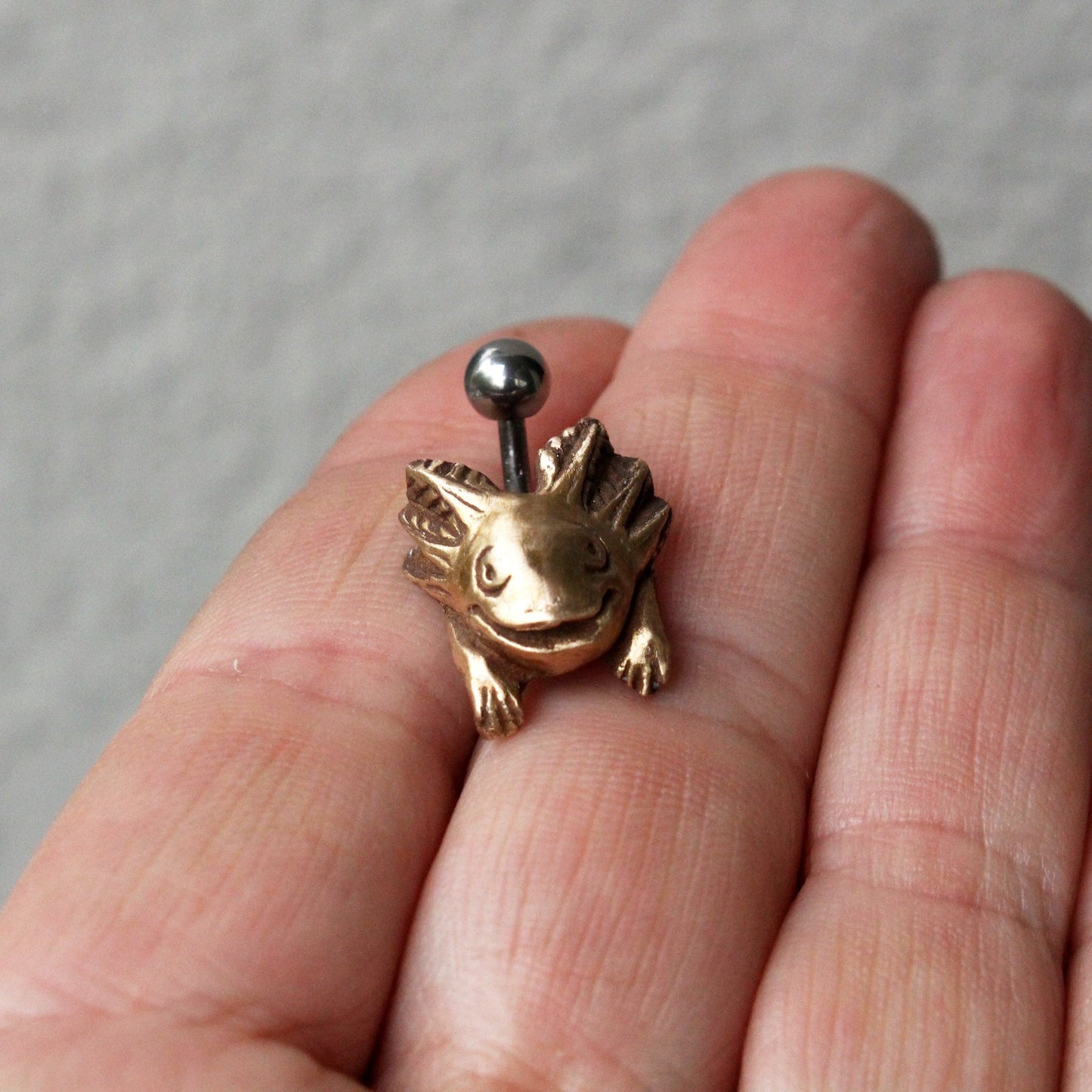 axolotlen navelpiercing i titan och brons, mexikansk salamandel, i handen på någon