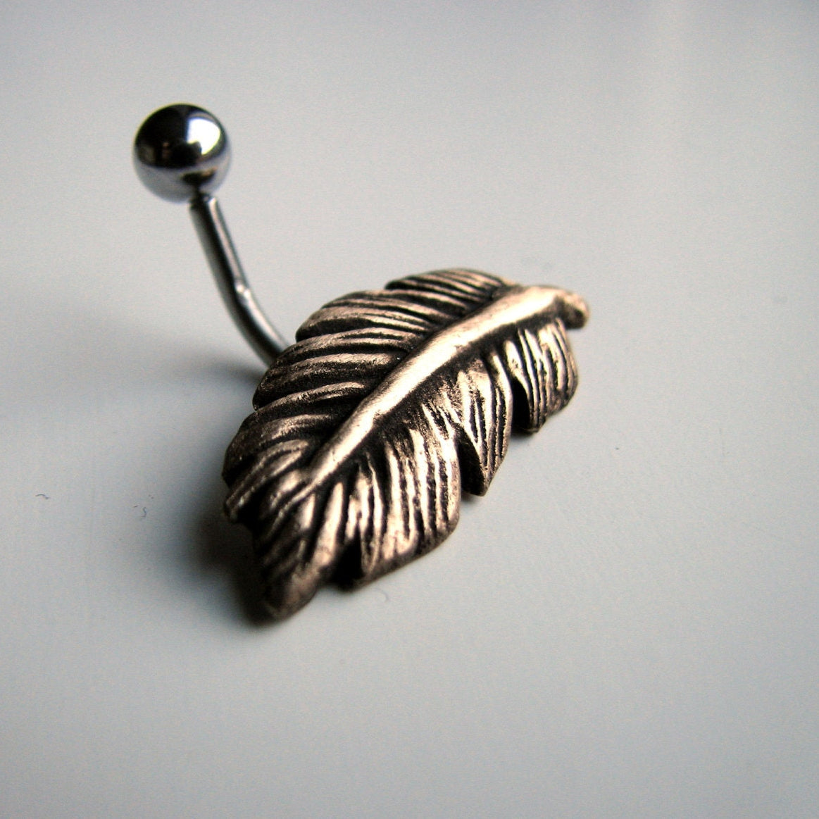 navelpiercing smycke med skulpterad fågel fjäder i brons