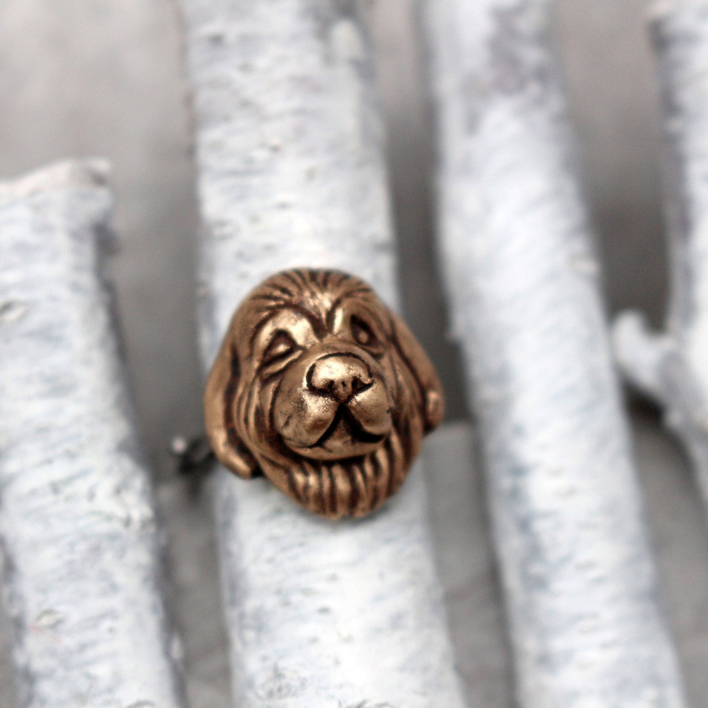 An adjustable ring with a bronze newfoundlander dog face set on a stainless steel band, displayed on a textured grey surface.