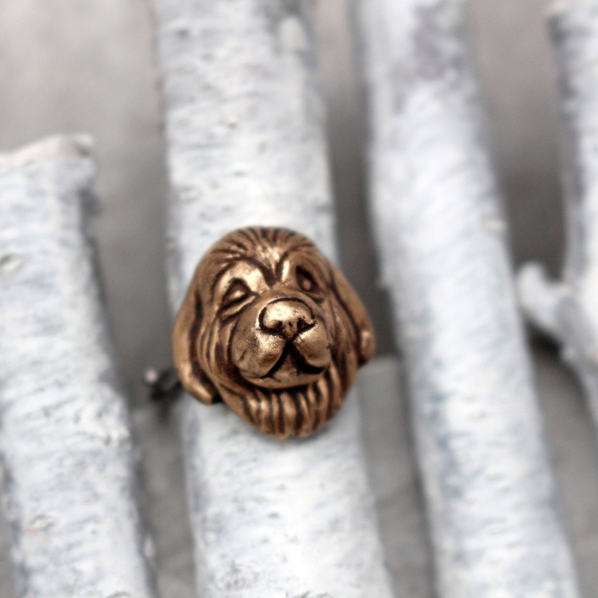 An adjustable ring with a bronze newfoundlander dog face set on a stainless steel band, displayed on a textured grey surface.