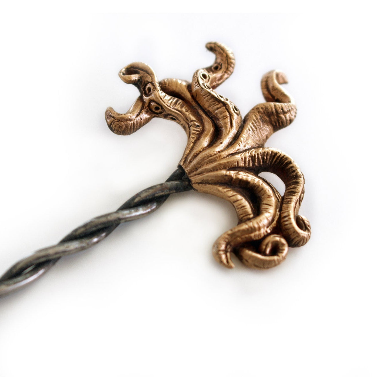 A bronze-colored octopus tentacle hair stick on a white background, with the stick partially embedded in the bronze sculpture.