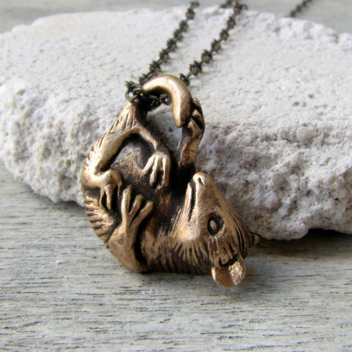 A bronze-colored metal pendant in the shape of a baby opossum