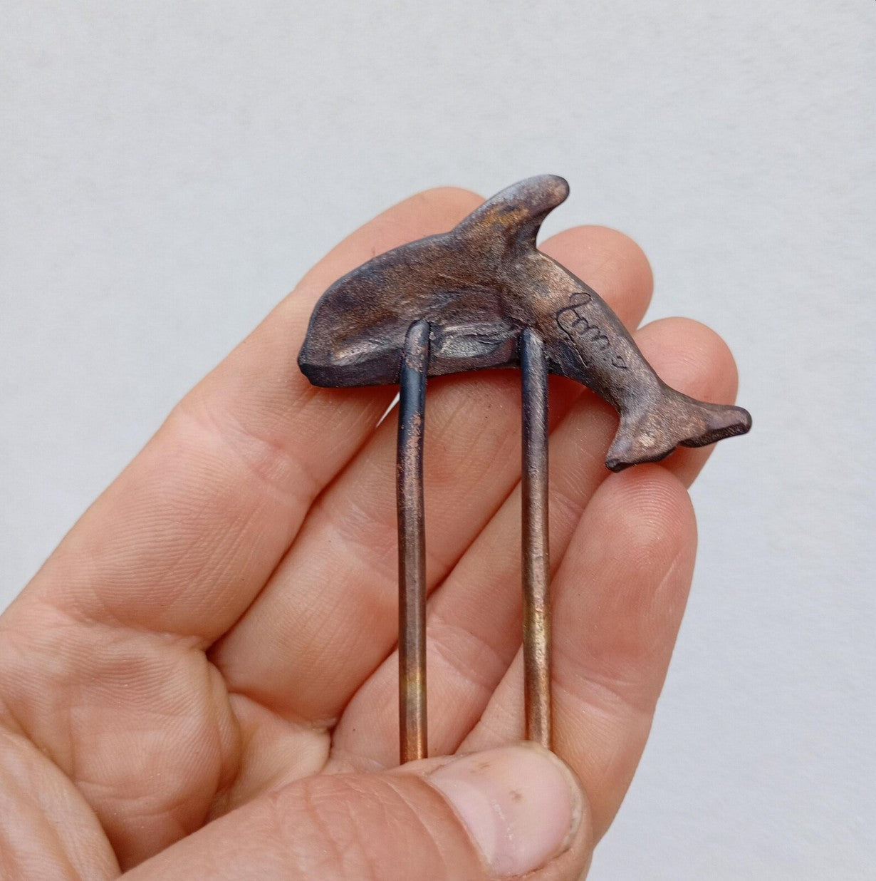 Hand holding a small metal sculpture of a shark against a plain background