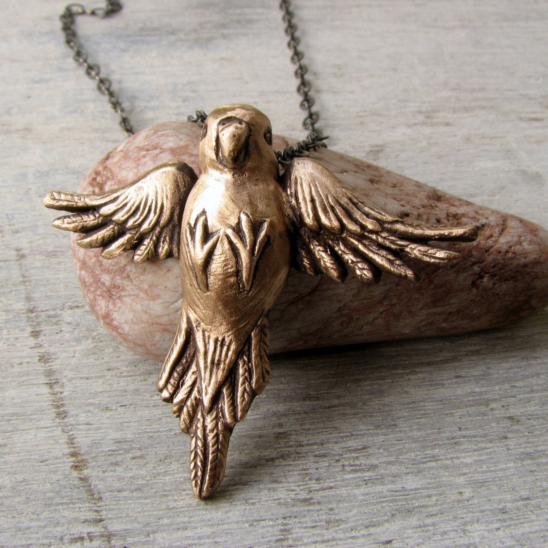 Bronze parakeet bird pendant necklace displayed on a gray background