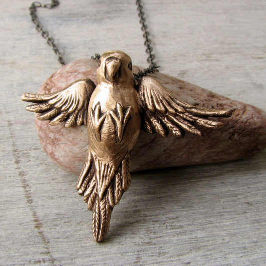 Bronze parakeet bird pendant necklace displayed on a gray background