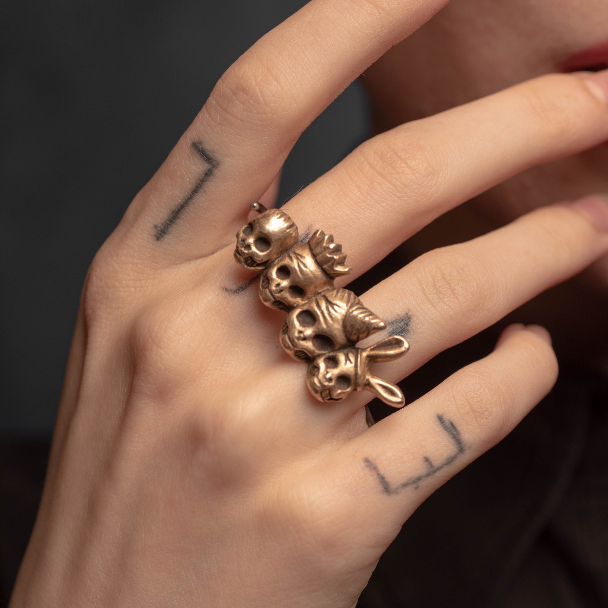 A hand wearing a gold-colored knuckle duster ring with four skull friends wearing party hats.