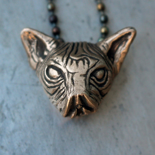 Bronze cat with a vulva for mouth pendant on a chain against a gray background