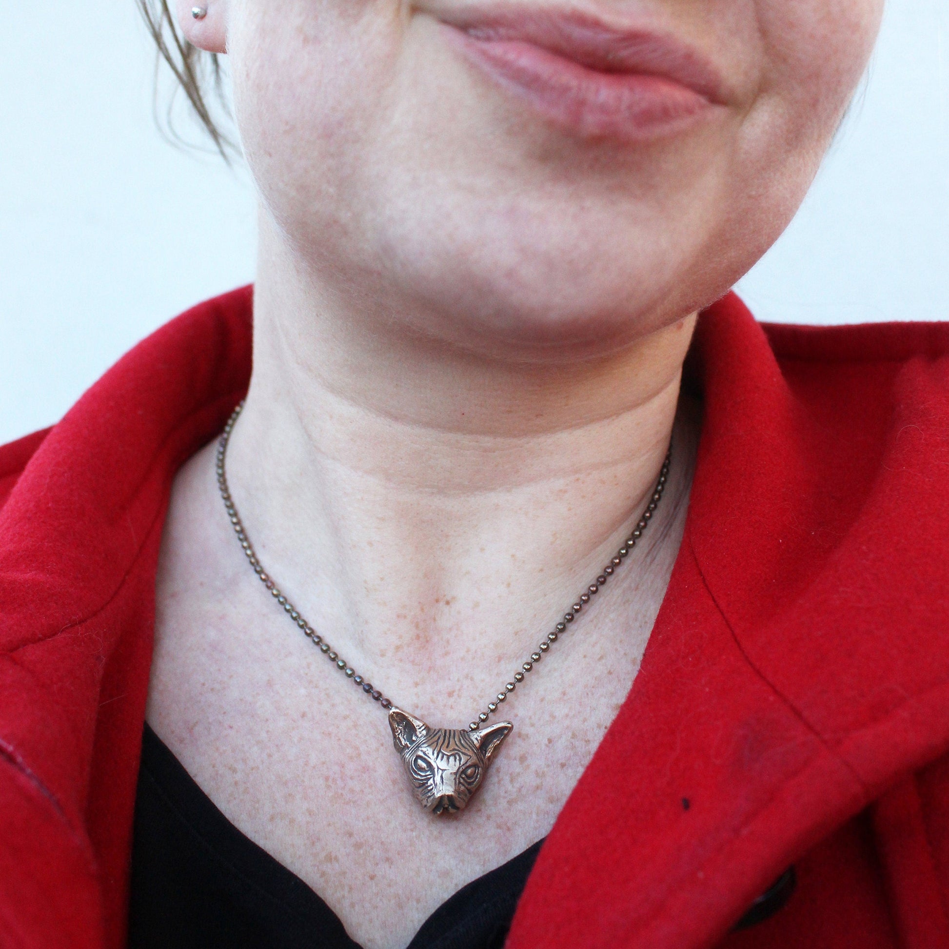 Person wearing a necklace with a kinky pussycat head pendant against a red garment.